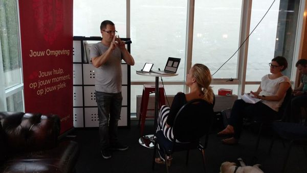 Johan Groskamp is standing in front of a presentation screen. An interpreter is seen sitting on the right.