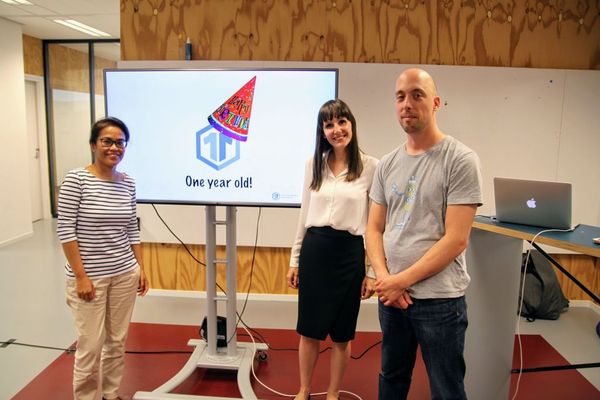 Eva Westerhoff, Irene Frijns and Job van Achterberg are standing in front of a presentation slide, showing the idea11y logo wearing a party hat, and the text "one year old!"